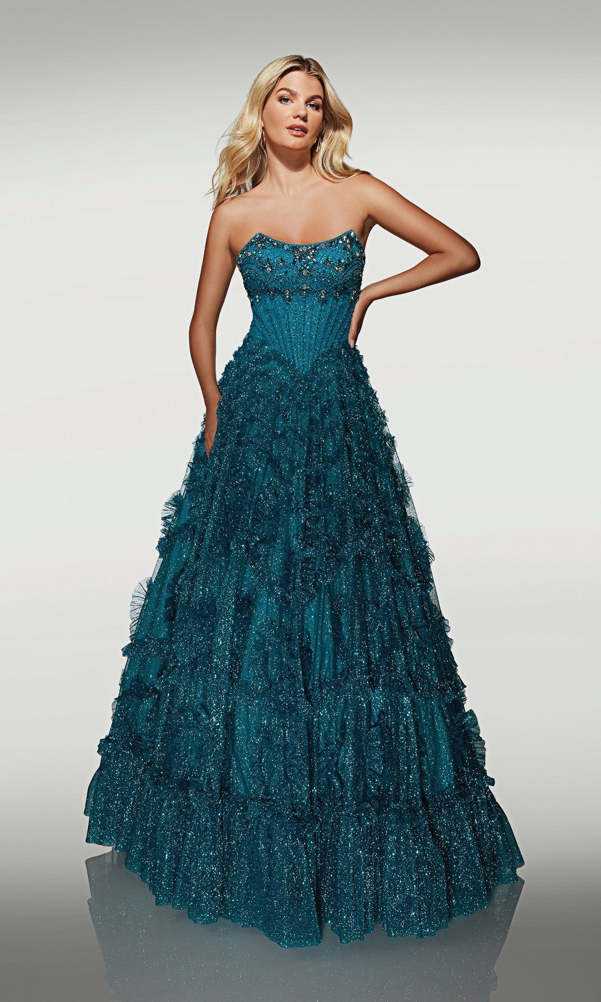 A woman wears the Alyce 62132 long formal dress in Caribbean, featuring a strapless neckline, layered ruffles, and a glitter tulle skirt. The gown shimmers elegantly against a plain background.